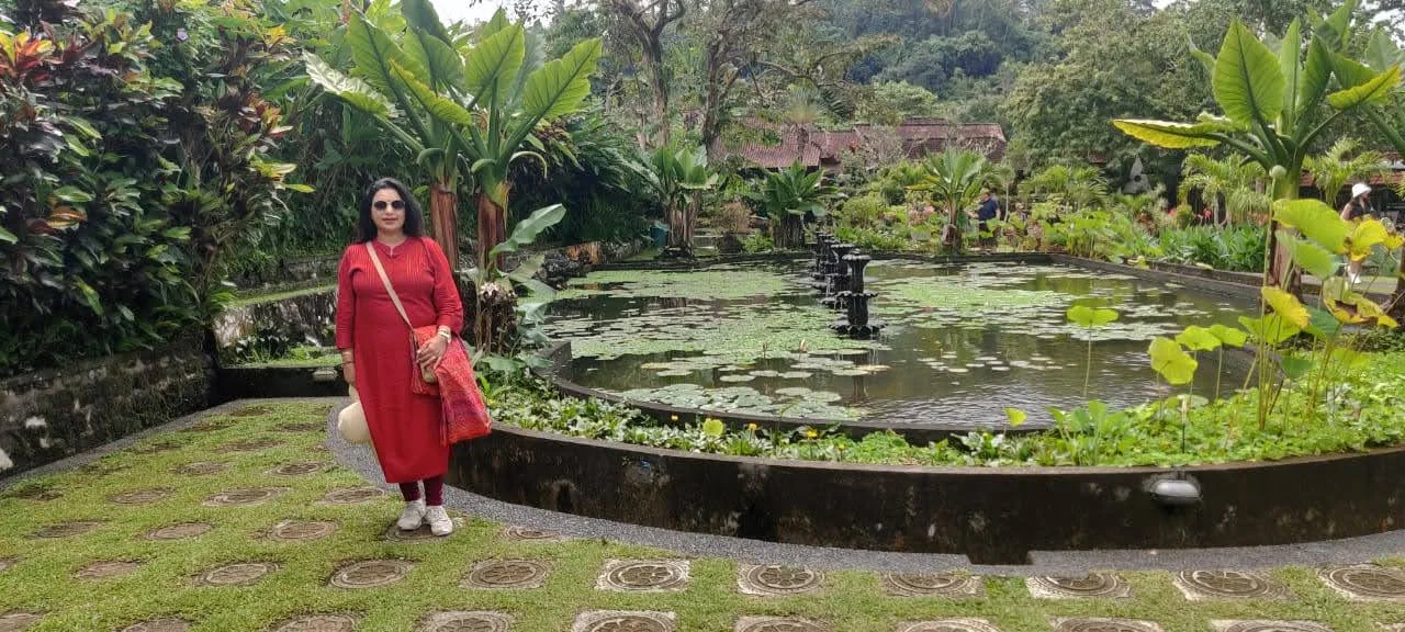Traveler standing beside the circular lily pond and water fountain at Taman Tirta Gangga surrounded by tropical flora