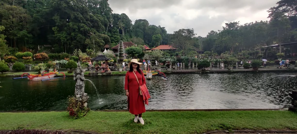 Panoramic view of Taman Tirta Gangga water palace with dragon boats and lush tropical hill backdrop in Bali