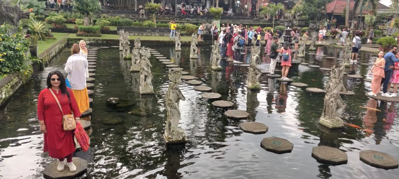 Traveler standing on sacred polygonal stepping stones above the lotus pool at Taman Tirta Gangga in Bali