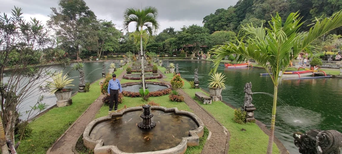 Traveler standing on the central path between reflection ponds and fountains at Taman Tirta Gangga