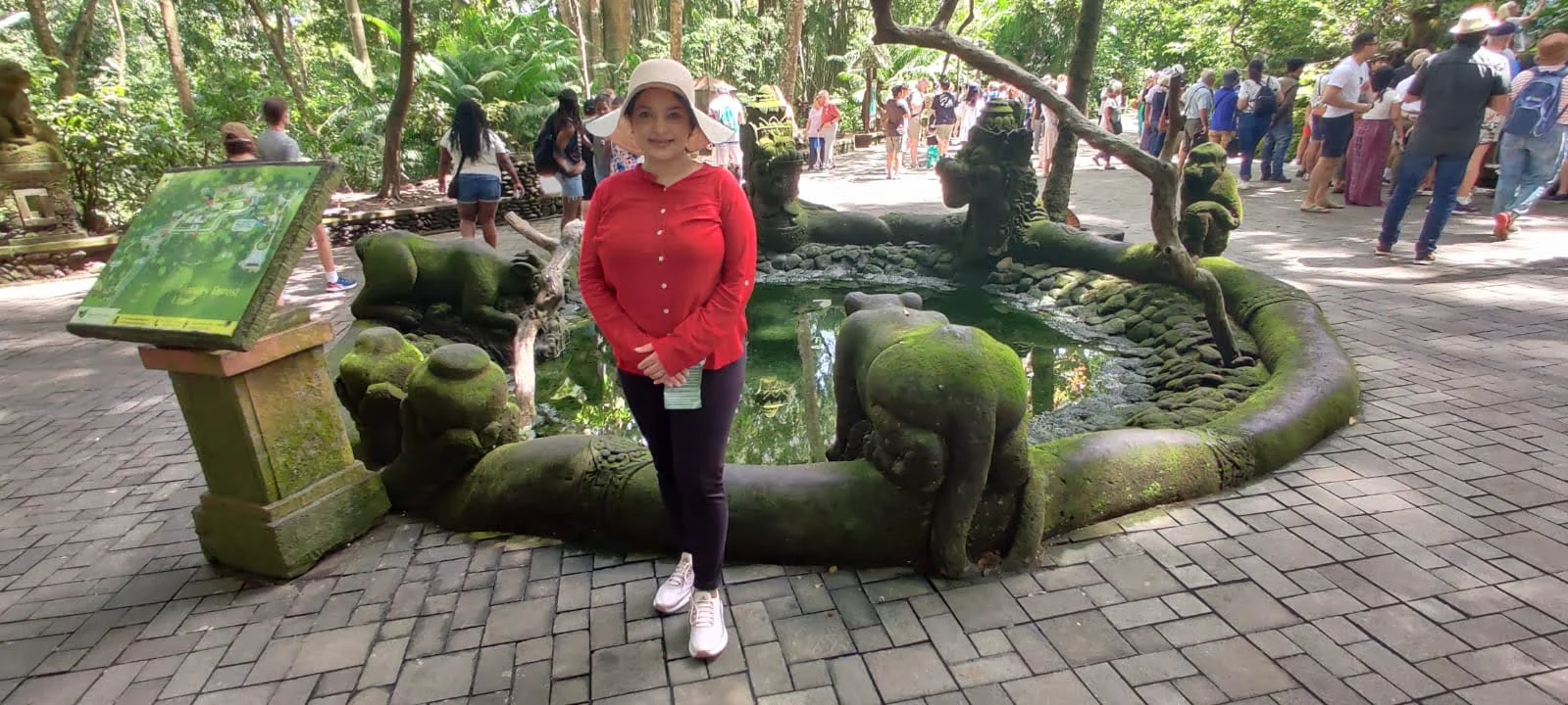 Lady traveler before the sacred moss-clad monkey fountain pool in the heart of the tropical forest sanctuary