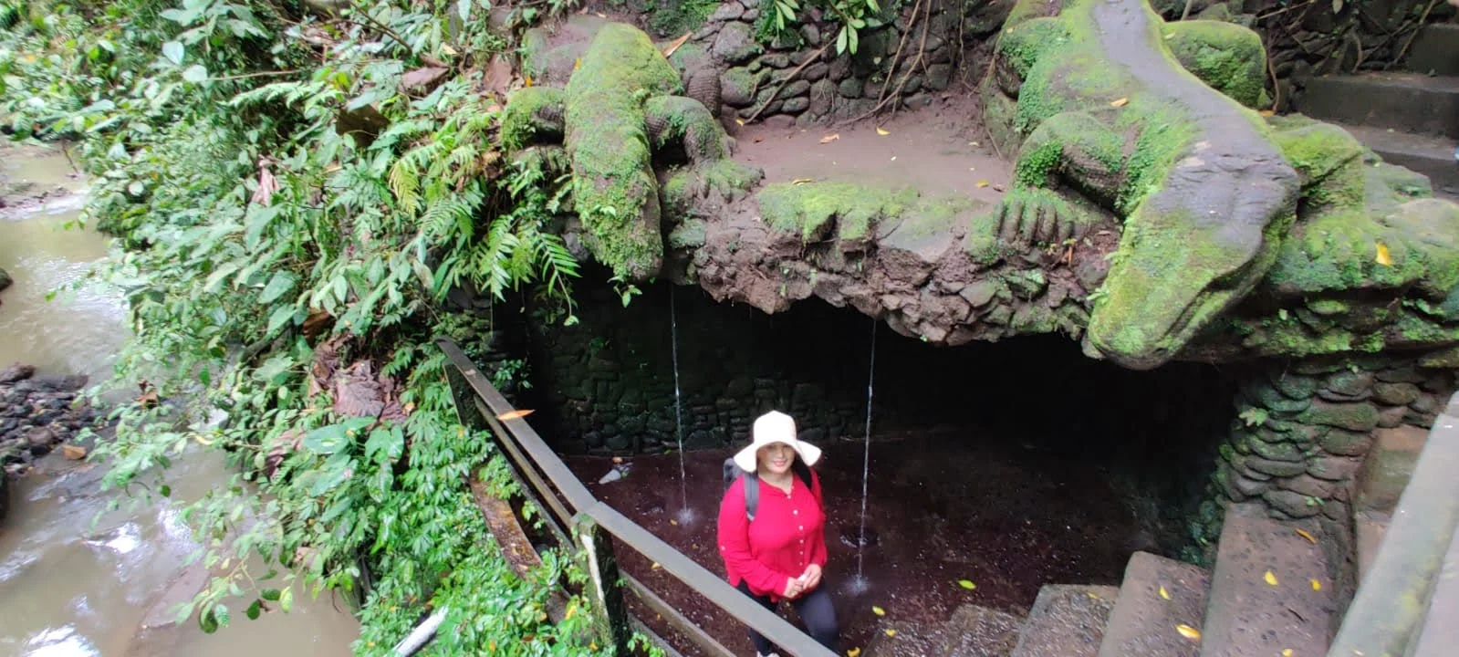 Lady traveler below twin carved stone dragon spouts cascading holy water into the river gorge below