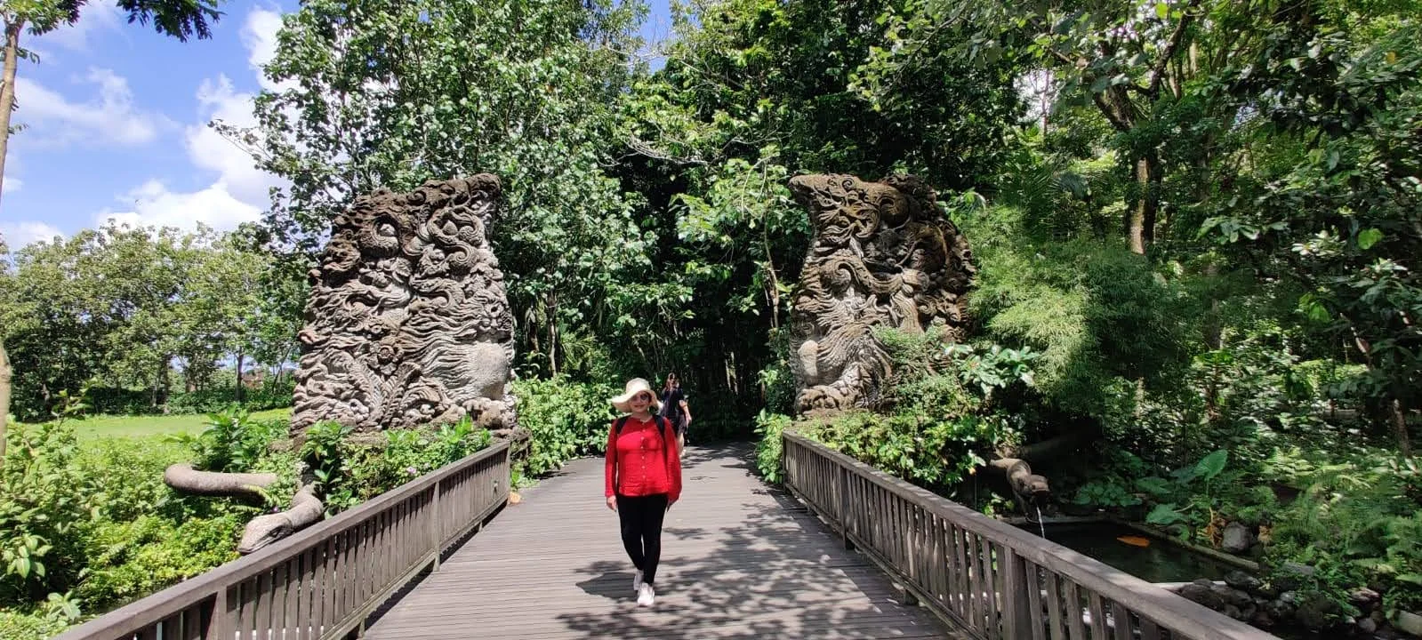 Lady traveler crossing the wooden forest bridge flanked by monumental carved stone mythical guardian portals
