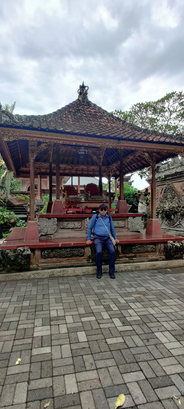 Gentleman traveler seated on the raised stone plinth of an open-air Bale pavilion with carved pillars at Ubud Palace
