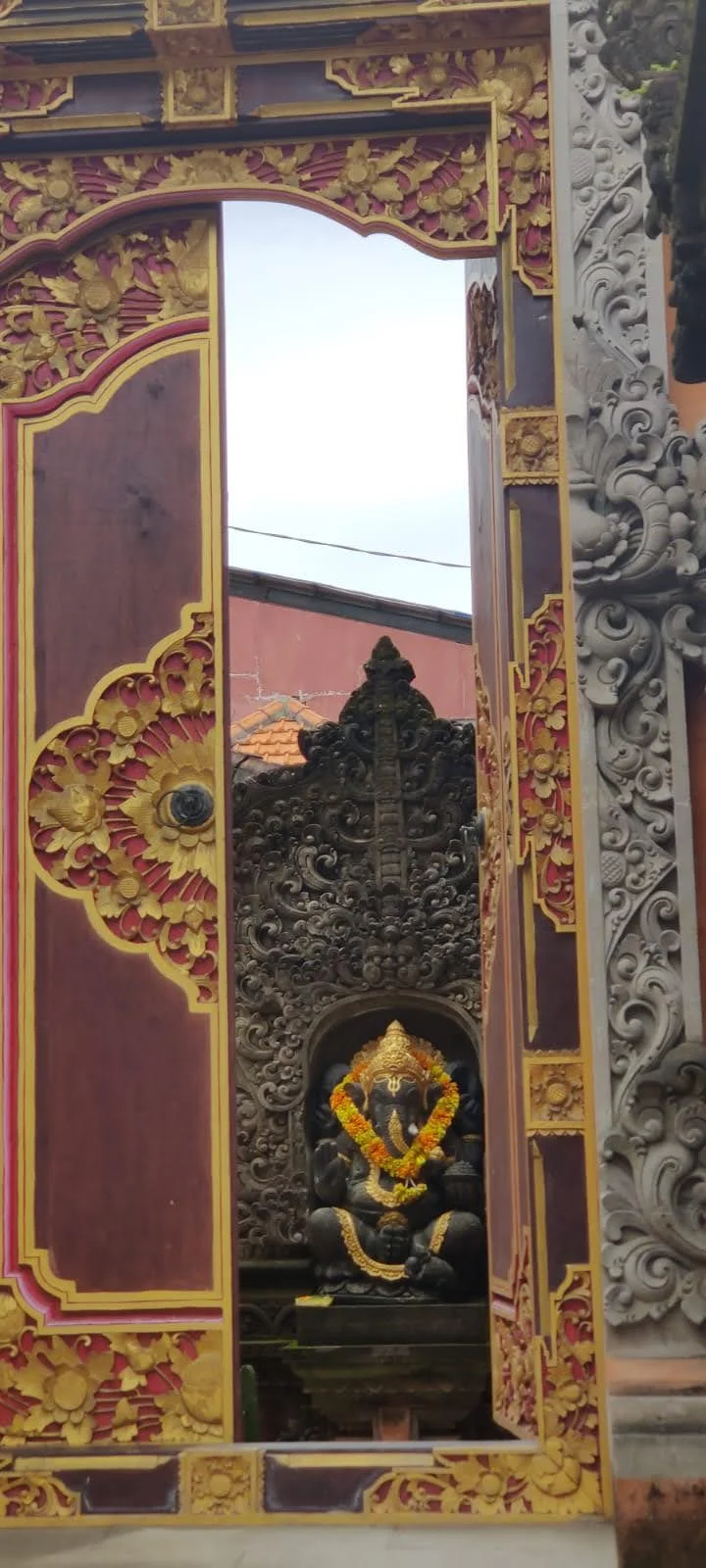 Carved gilded doorway framing an inner sanctum shrine of Lord Ganesha crowned in gold and draped in yellow flower garlands