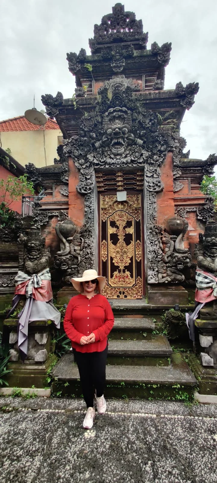 Lady traveler before the monumental Kori Agung stone portal with gilded floral doors and carved Bhoma face at Ubud Palace