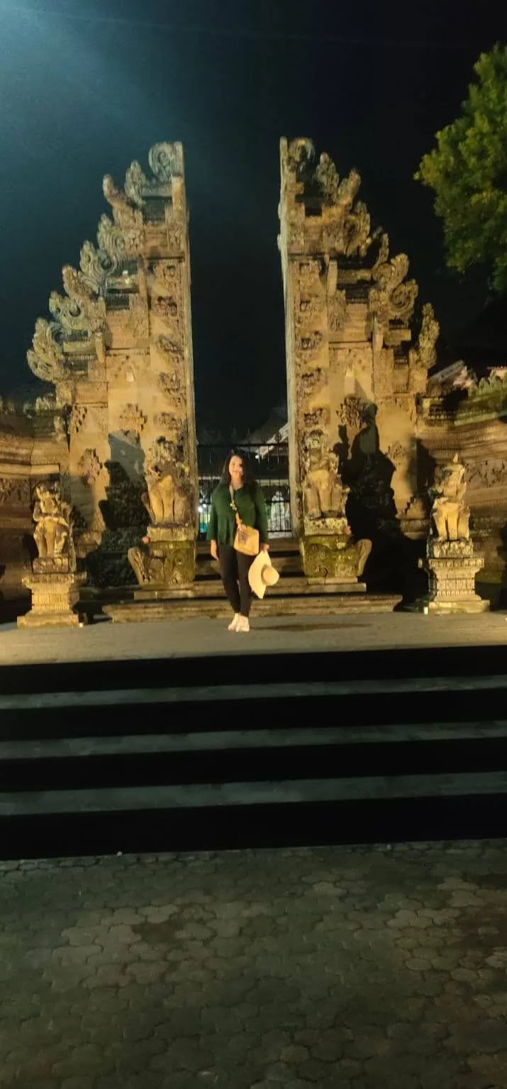 Lady traveler before the illuminated grand Candi Bentar split gate of Puri Saren Agung at night
