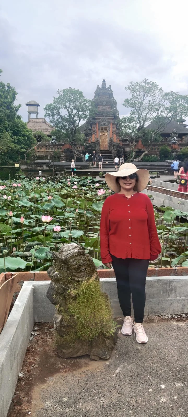 Lady traveler beside an ancient mossy stone guardian overlooking the lotus blooms at Saraswati Temple