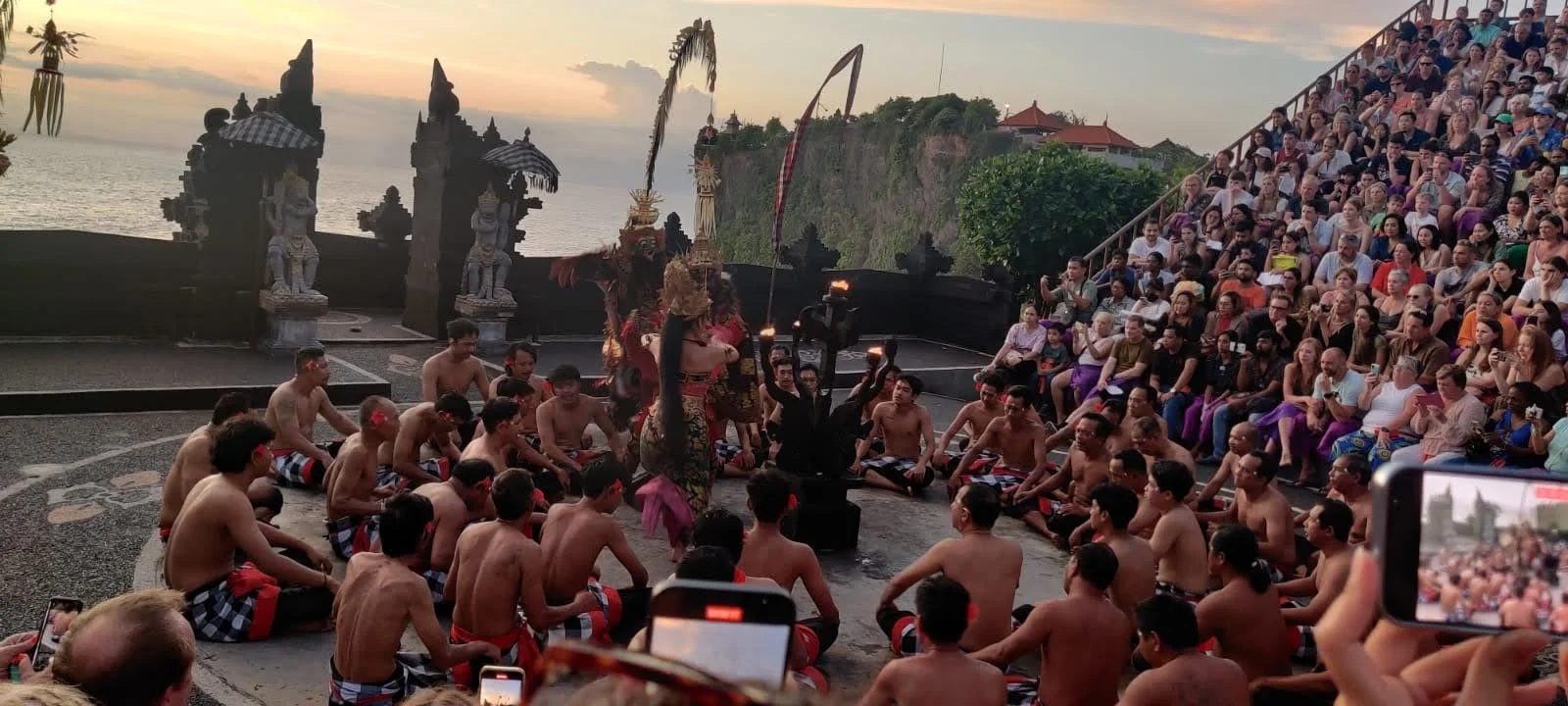 Men seated in concentric circles chanting cak, cak, cak in hypnotic rhythm as sunset approaches at Uluwatu amphitheatre