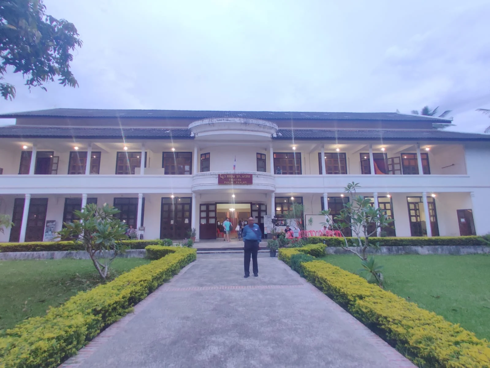 Traveler standing in front of the Royal Theatre building and palace garden in Luang Prabang