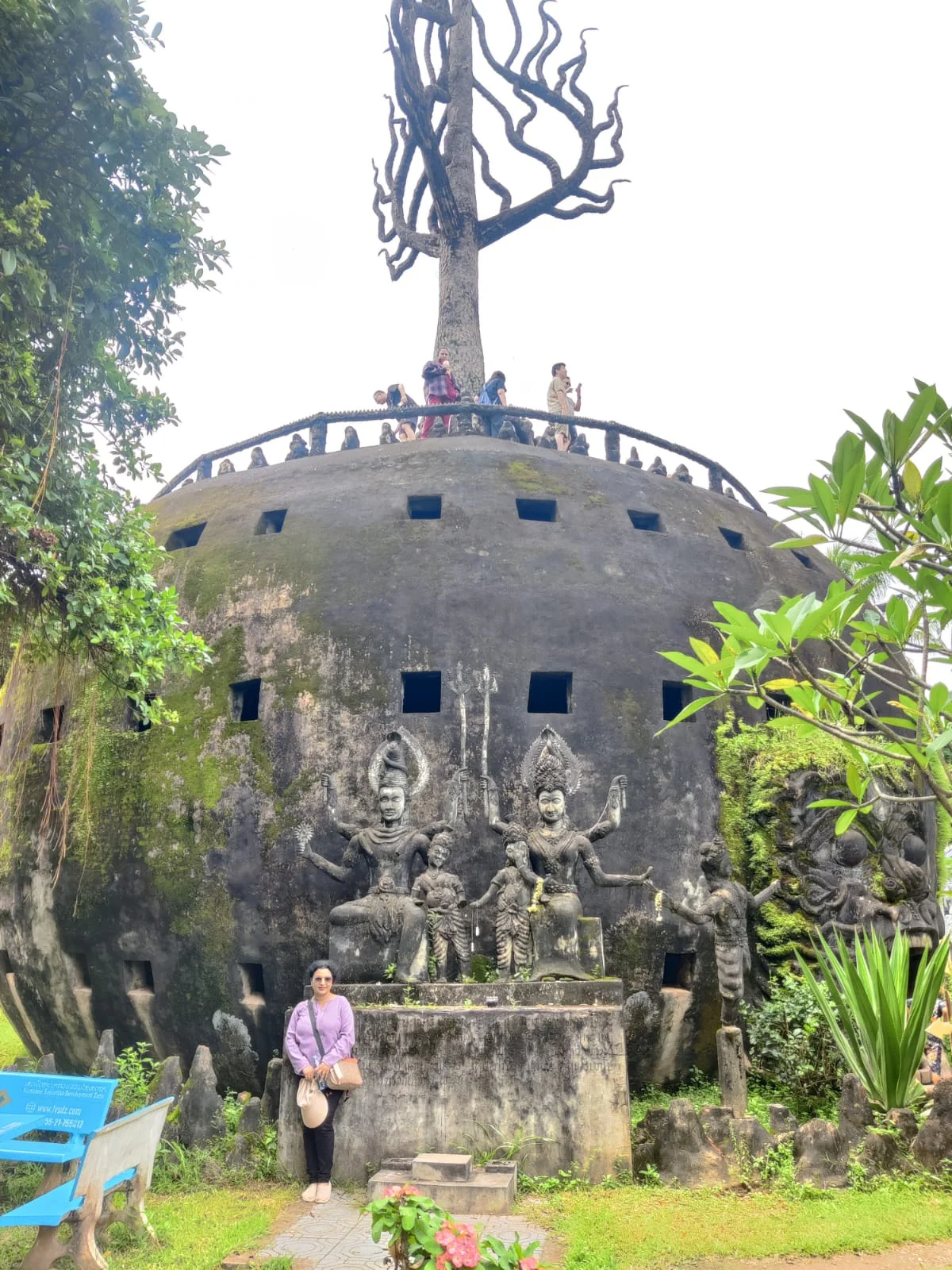 Traveler standing beside the monumental three-story pumpkin cosmic structure topped with a spire and stone statue of Shiva and Parvati