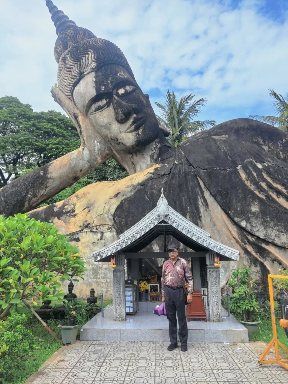 Traveler standing respectfully alongside the colossal 40-metre reclining Buddha statue in Xieng Khuan