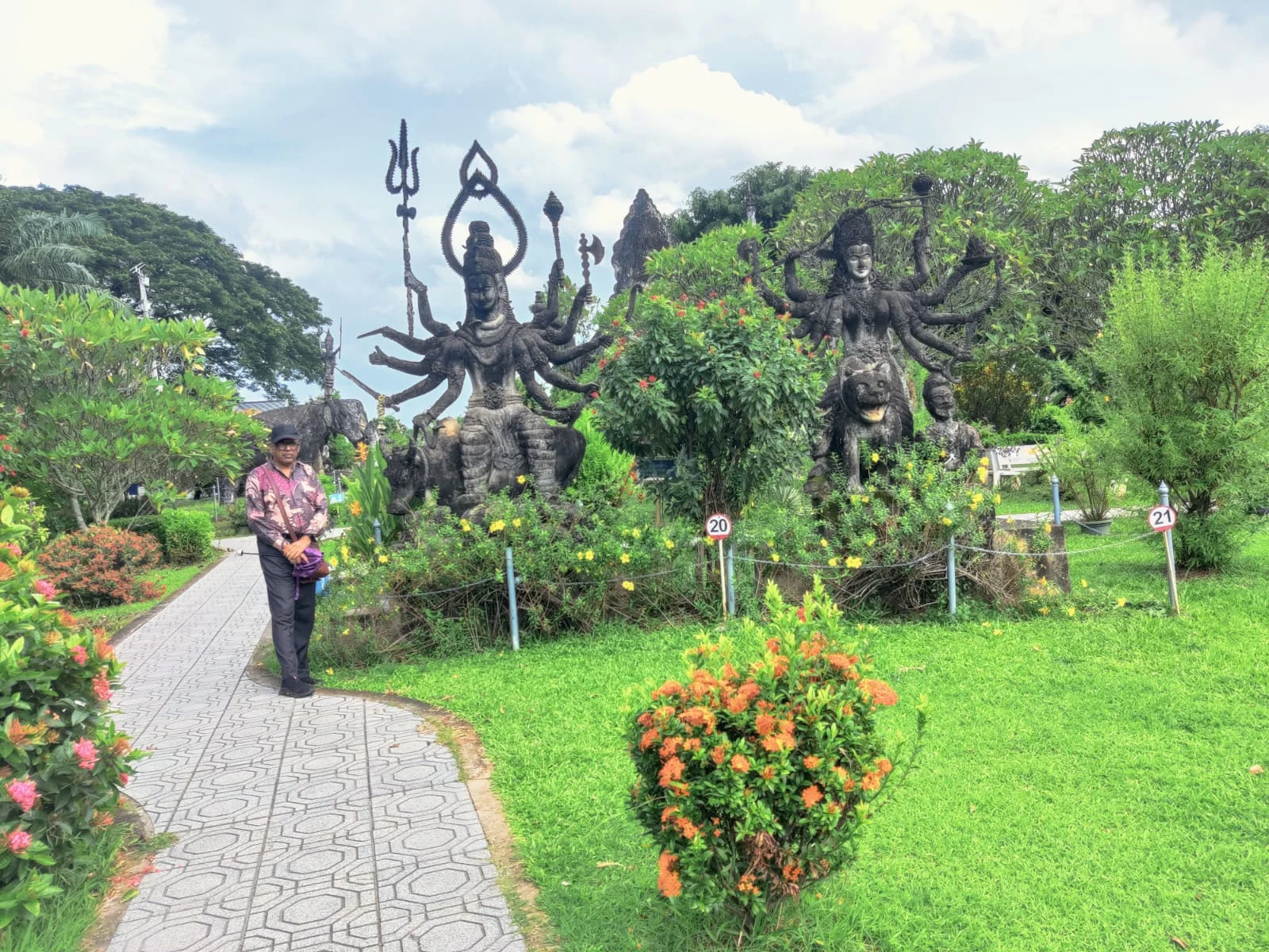 Traveler standing before concrete sculptures of Lord Shiva with the trident riding Nandi bull and Goddess Durga astride her lion at Buddha Park