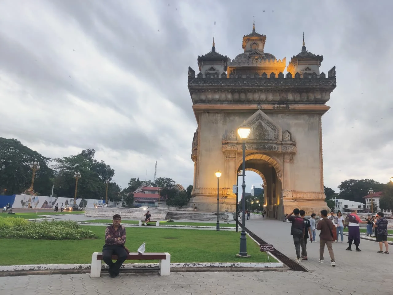 Traveler admiring the evening illumination of Patuxai with musical fountains glowing in front of the illuminated monument
