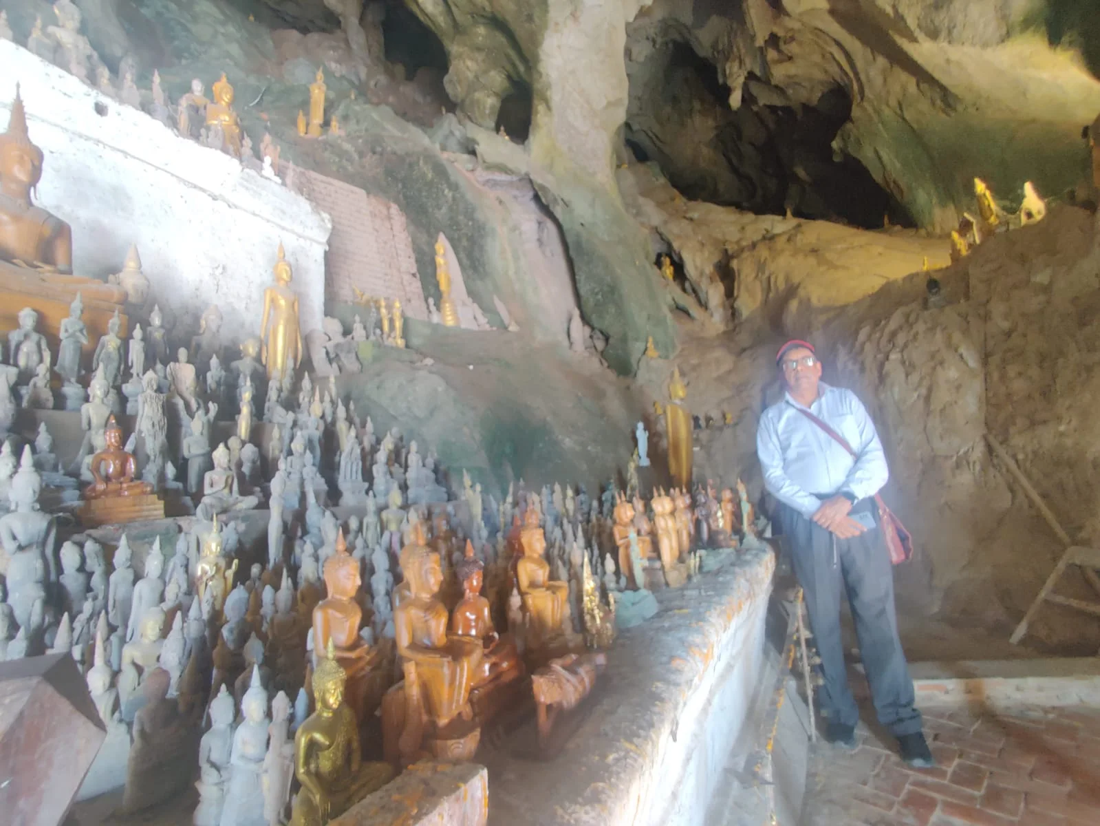Male traveler exploring the rock shelves of Pak Ou Caves filled with hundreds of historical wooden Buddha statues