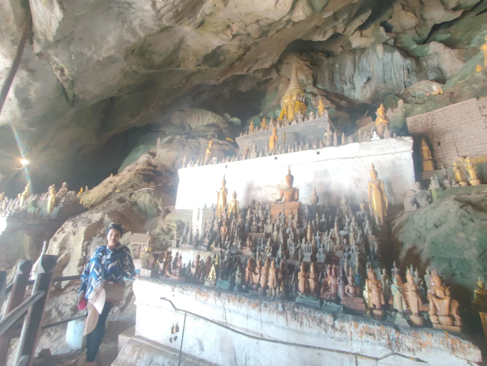 Wide perspective looking out from Tham Ting cave entrance over the swirling Mekong and Nam Ou rivers with Buddha statues along the limestone precipice
