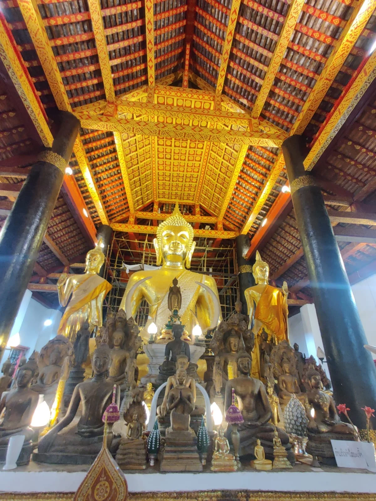 Wat Wisunarat grand sanctuary altar with colossal golden Buddha image surrounded by historic bronze statues and ceremonial umbrellas