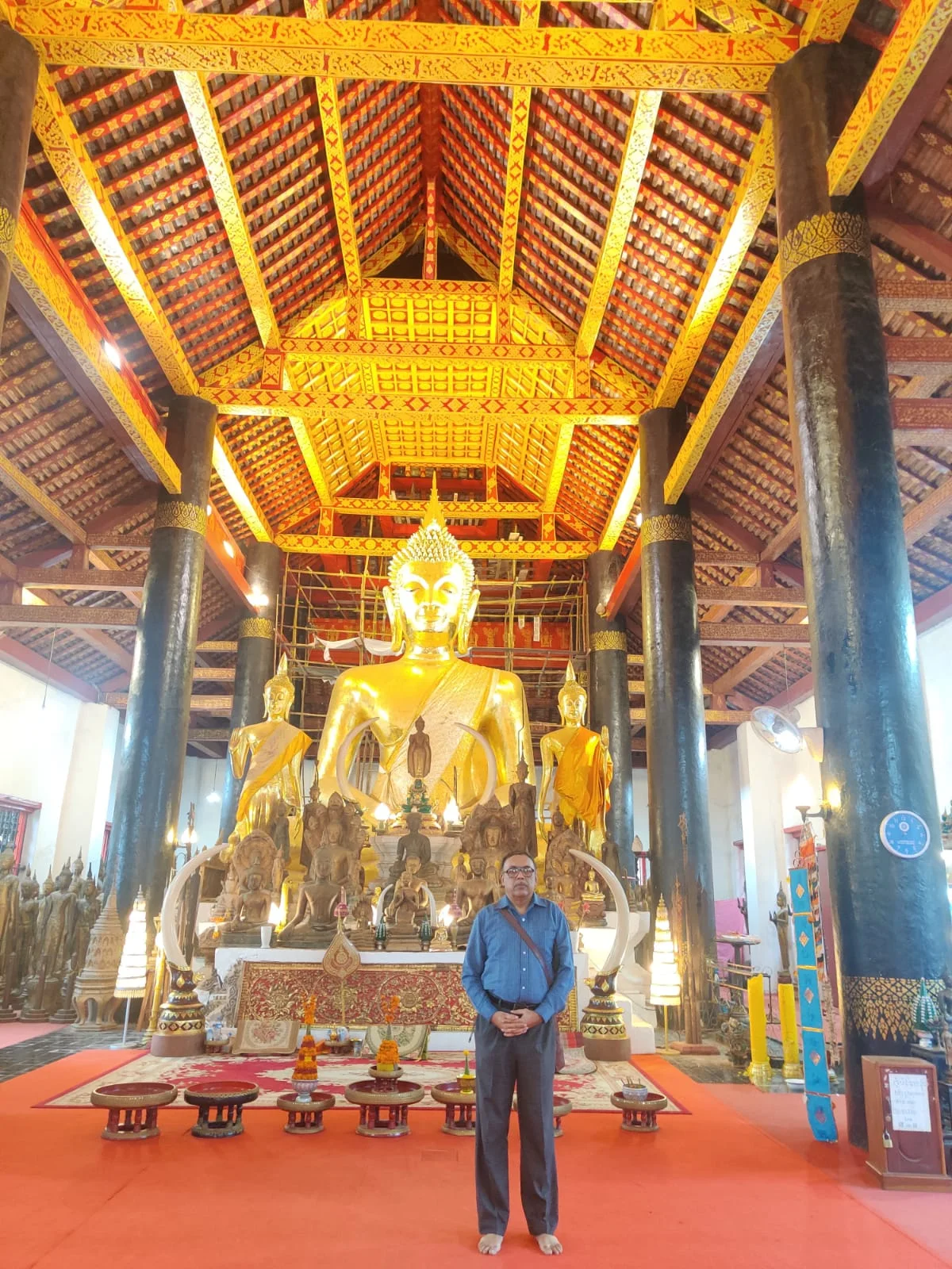 Male traveler inside Wat Wisunarat (Wat Visoun) standing beneath the colossal dark wooden timber beams and historic pillars