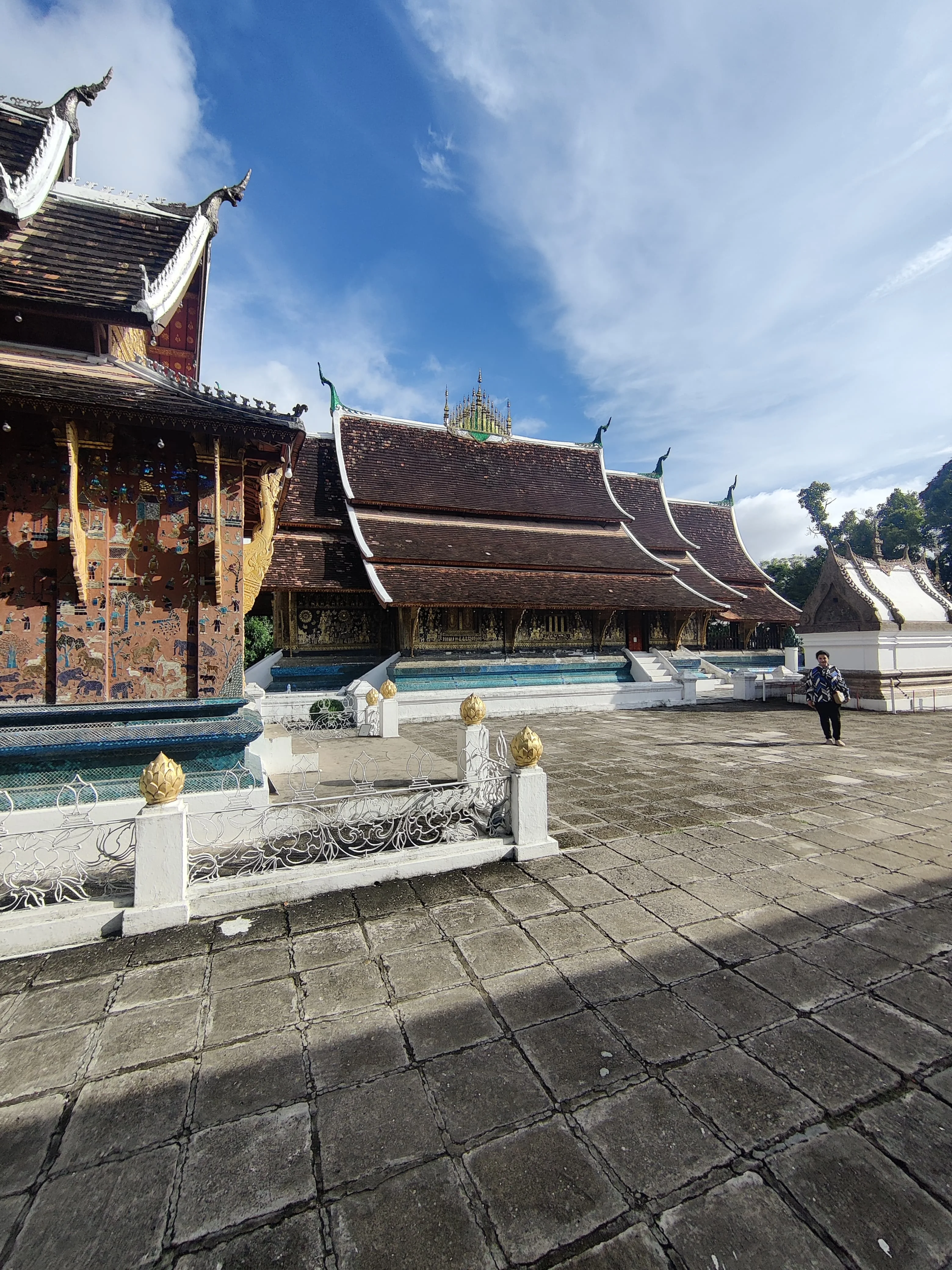 Courtyard of Wat Xieng Thong featuring the Red Chapel with Tree of Life colored glass mosaic and female traveler enjoying the sacred compound