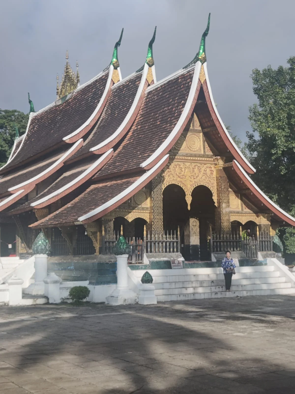 Female traveler admiring the dramatic low sweeping tiered roofline of Wat Xieng Thong in Luang Prabang