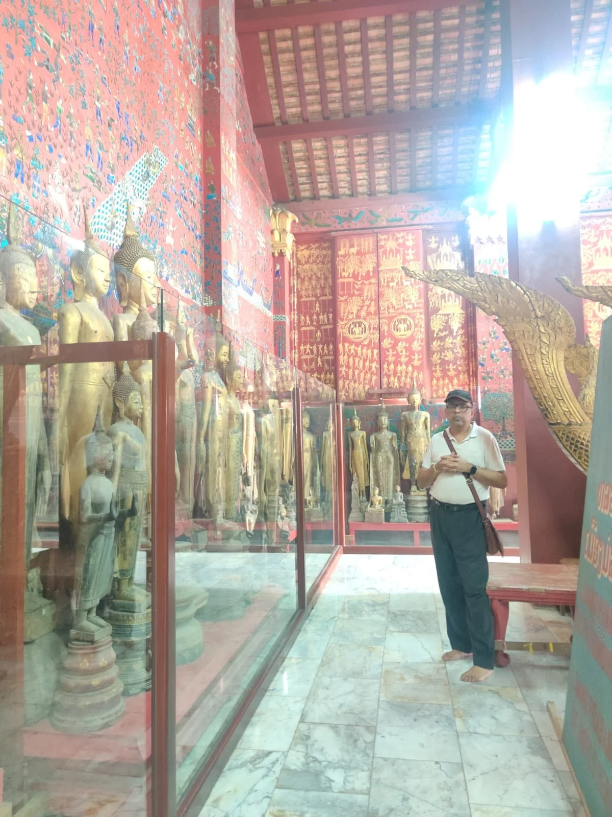 Male traveler in the Royal Funeral Chariot Hall at Wat Xieng Thong gazing at the colossal gilded teak carriage with seven-headed Naga heads