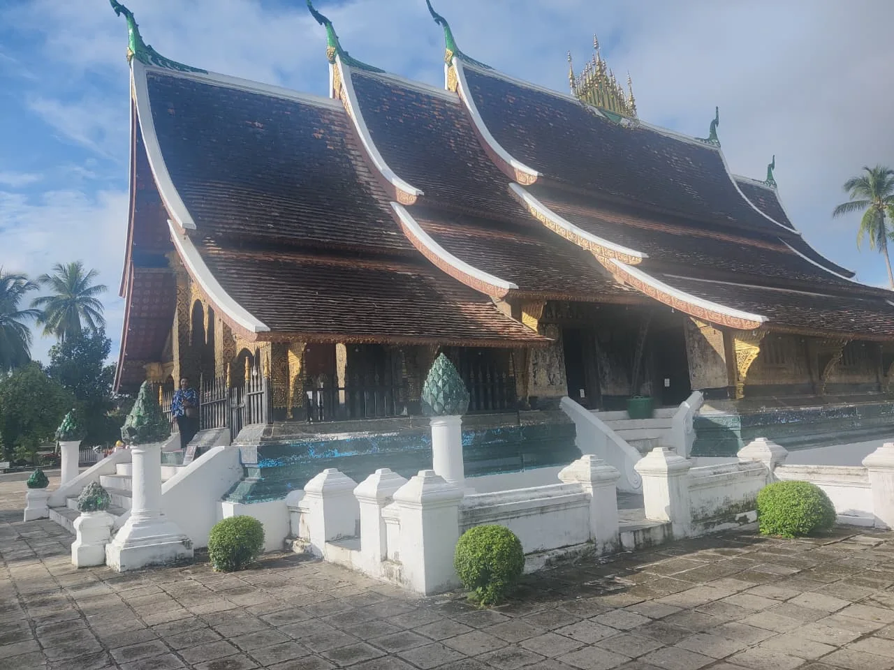 Exterior side elevation of the Sim at Wat Xieng Thong showing multi-tiered eaves, black lacquer walls with gold stenciling, and Dok So Fa spire finials