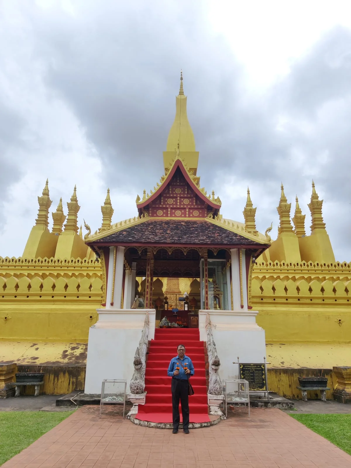 Male traveler walking up the red-carpeted grand staircase leading toward Pha That Luang in Vientiane