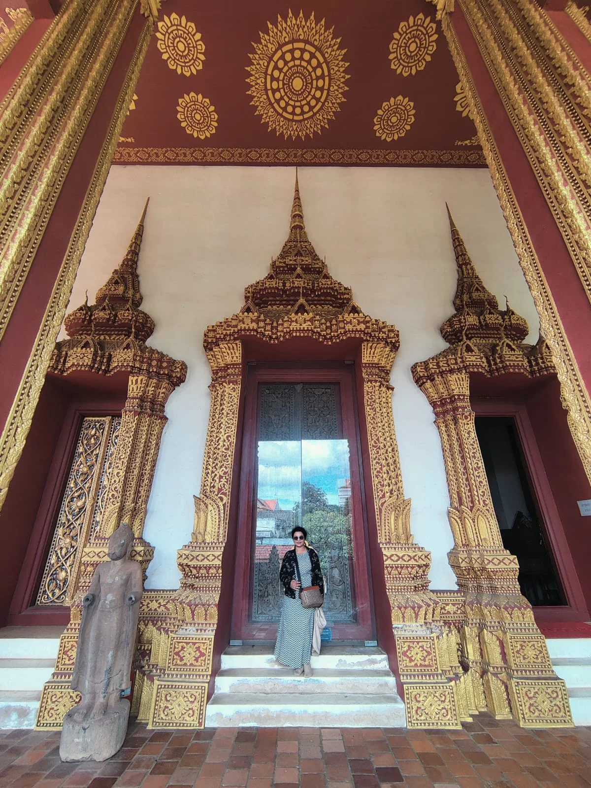 Female traveler standing beside the intricately carved and gilded teakwood entrance doorway of Wat Ho Phra Keo