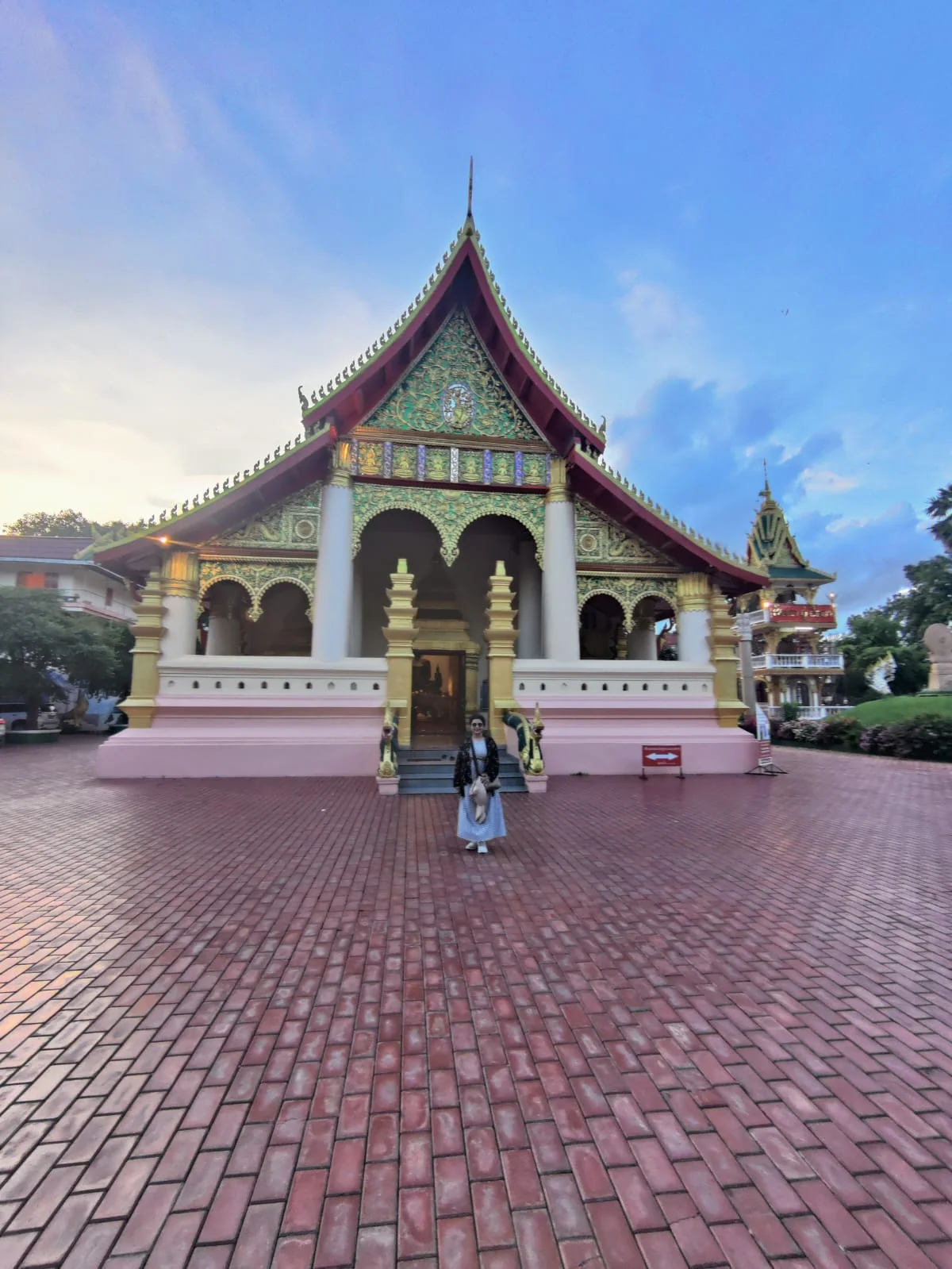 Female traveler in the peaceful courtyard of Wat Ong Teu Mahawihan shaded by palms and frangipani trees in Vientiane
