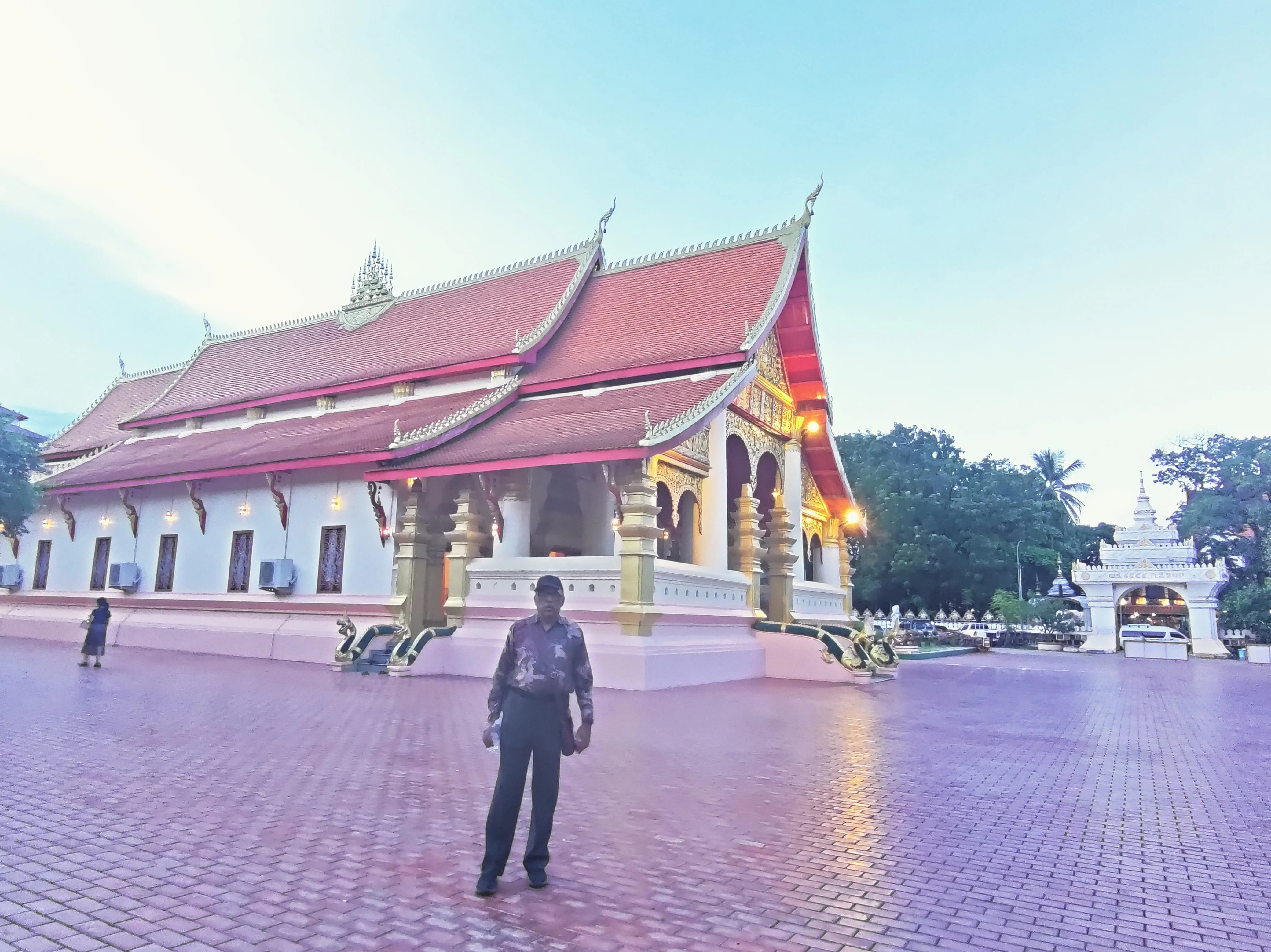 Male traveler standing outside Wat Ong Teu at twilight under glowing golden lanterns hanging along the monastery eaves