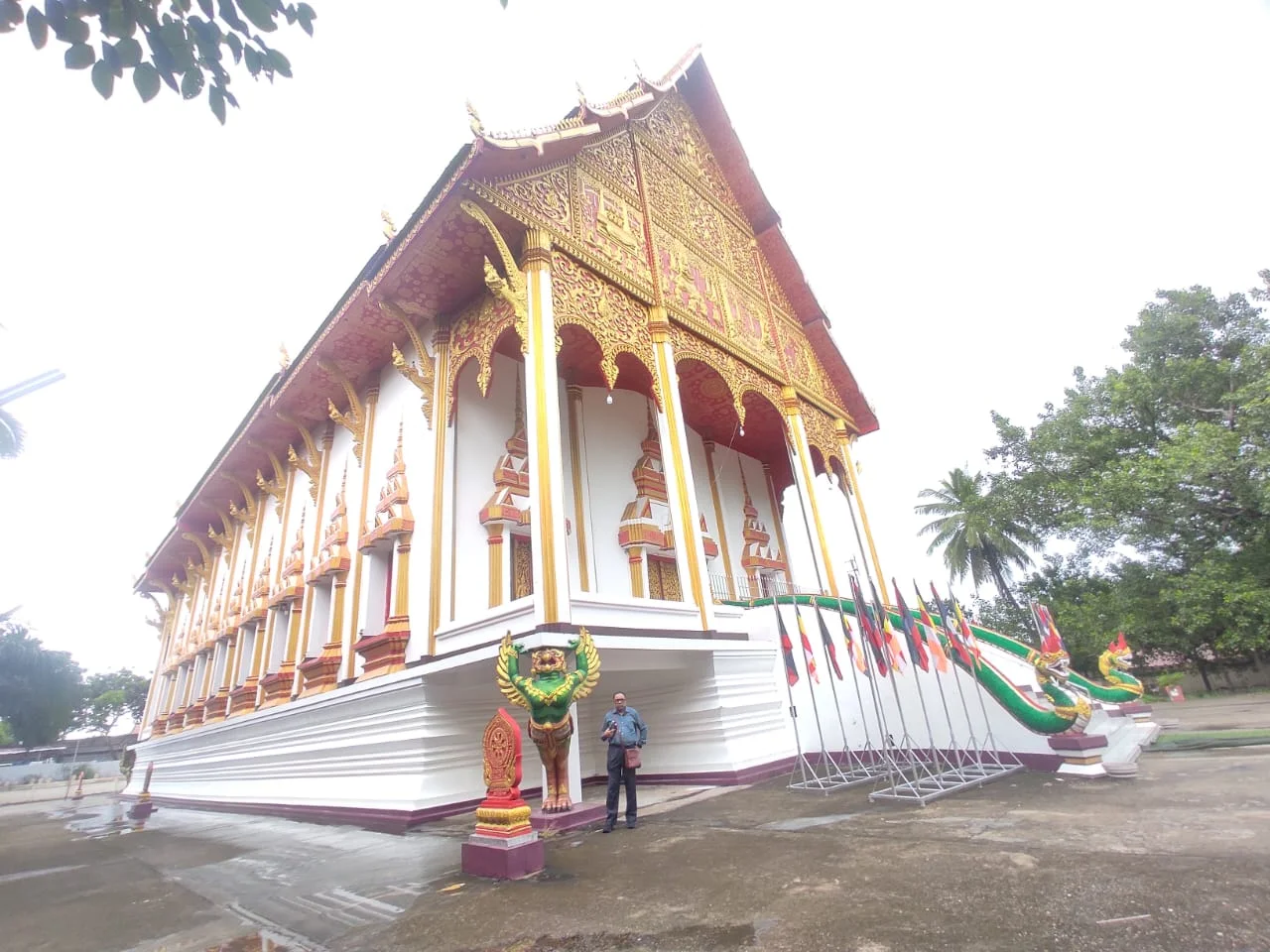 Male traveler standing in front of Wat That Luang Neua with ornate golden multi-headed Naga serpents and Garuda sculptures flanking the grand stairs