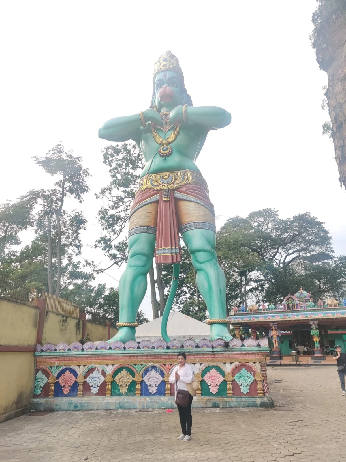 Female traveler admiring the 50-foot colossal green Hanuman statue framed against the limestone cliff canopy