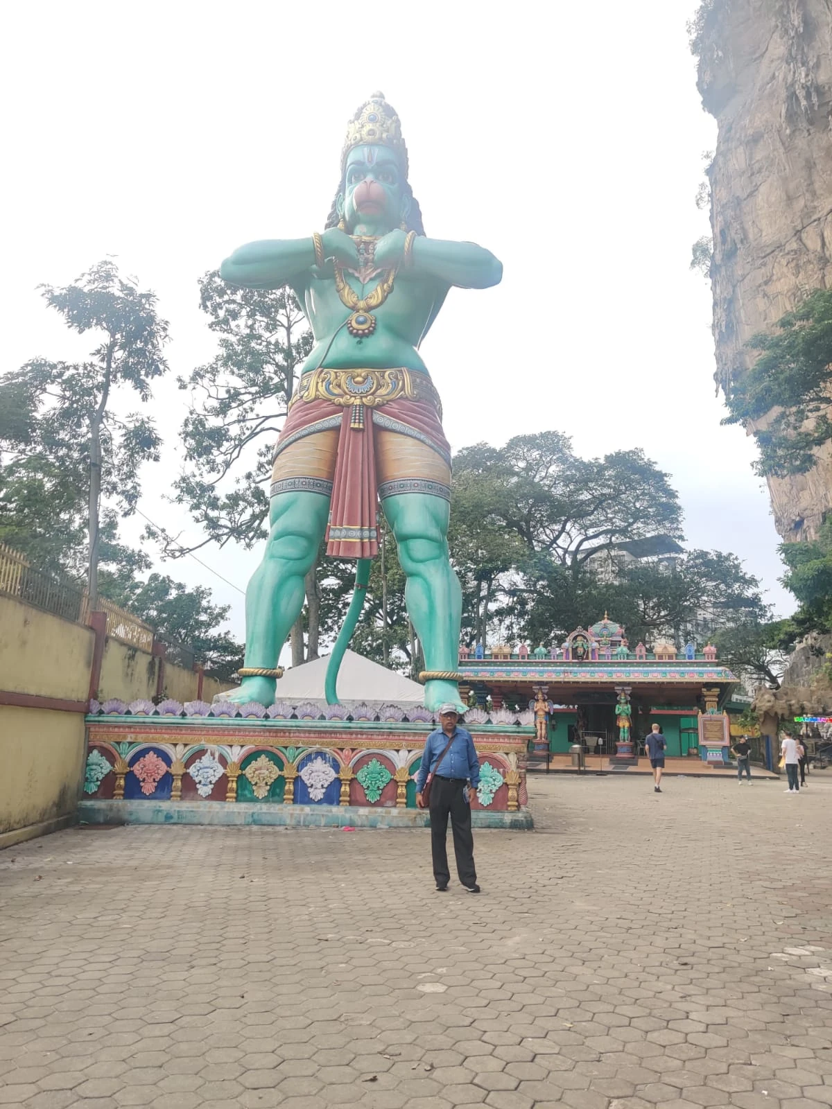Male traveler standing in awe before the 50-foot colossal emerald-green statue of Lord Hanuman at the Ramayana Cave entrance