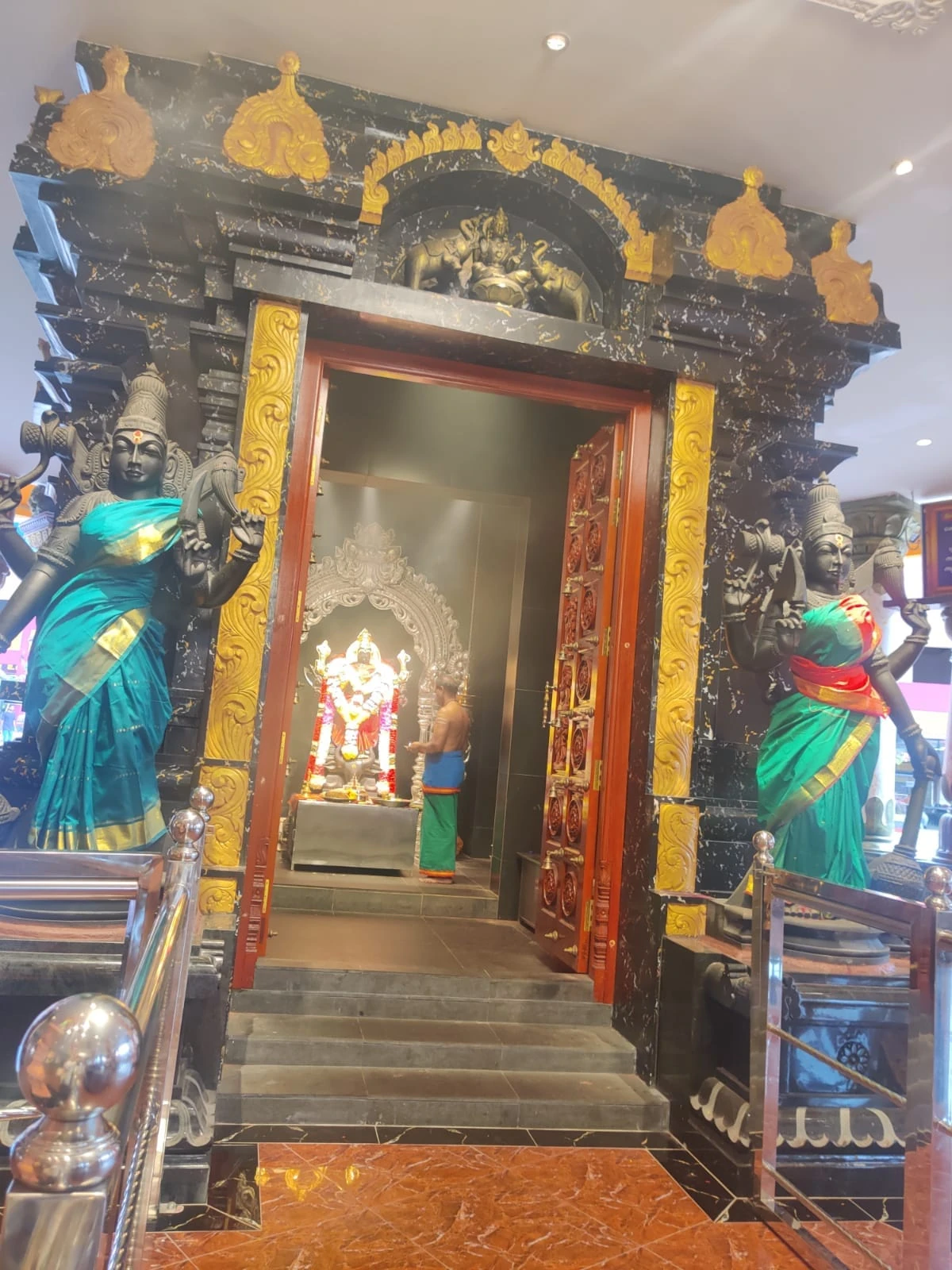 Hindu priest in traditional dhoti performing sacred puja before the sanctum flanked by dvarapalika guardian sculptures and brass oil lamps