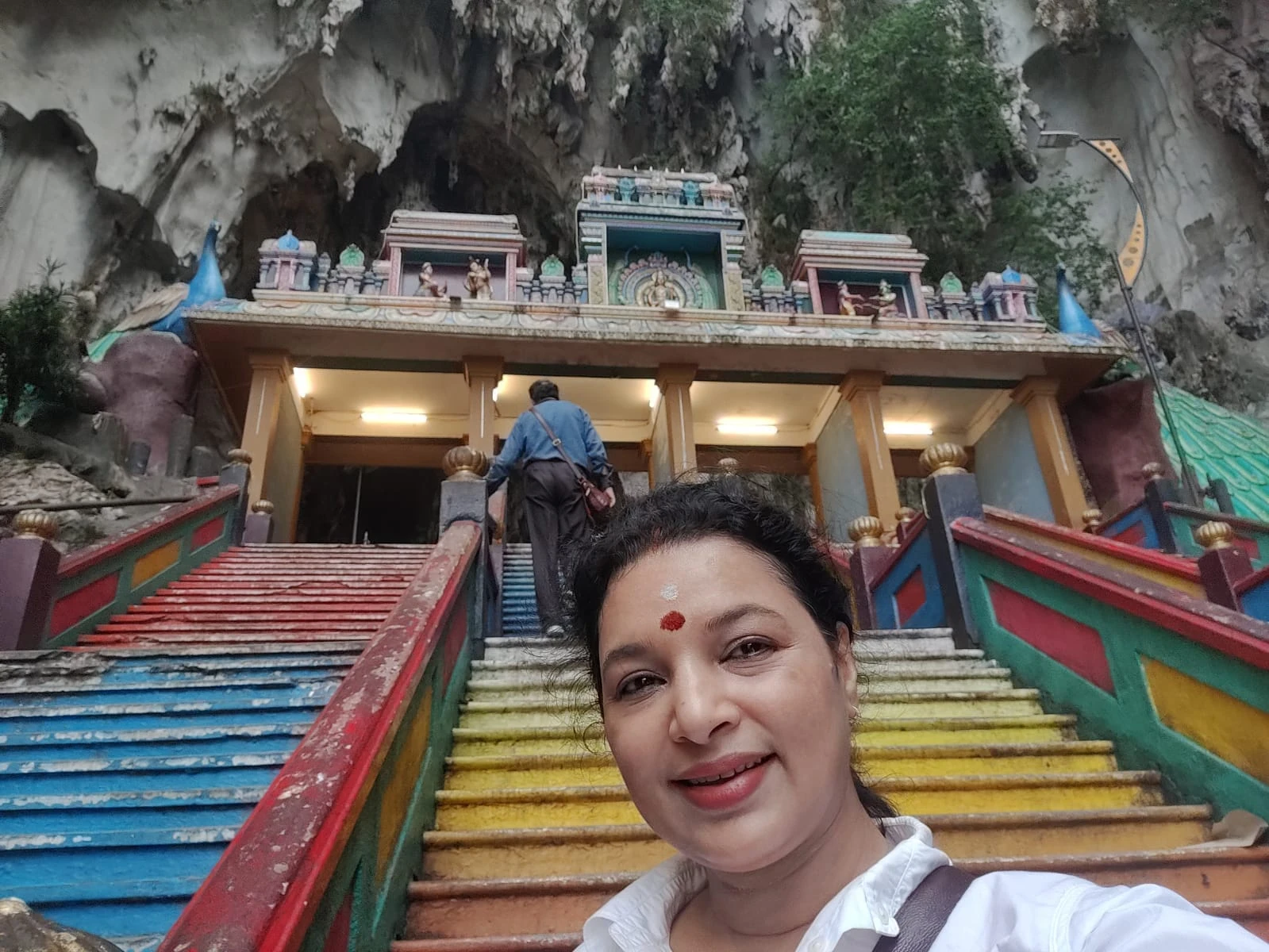 The vibrant 272 rainbow-painted staircase ascending into the sheer limestone cliff face behind the ornate South Indian entrance gopuram gate