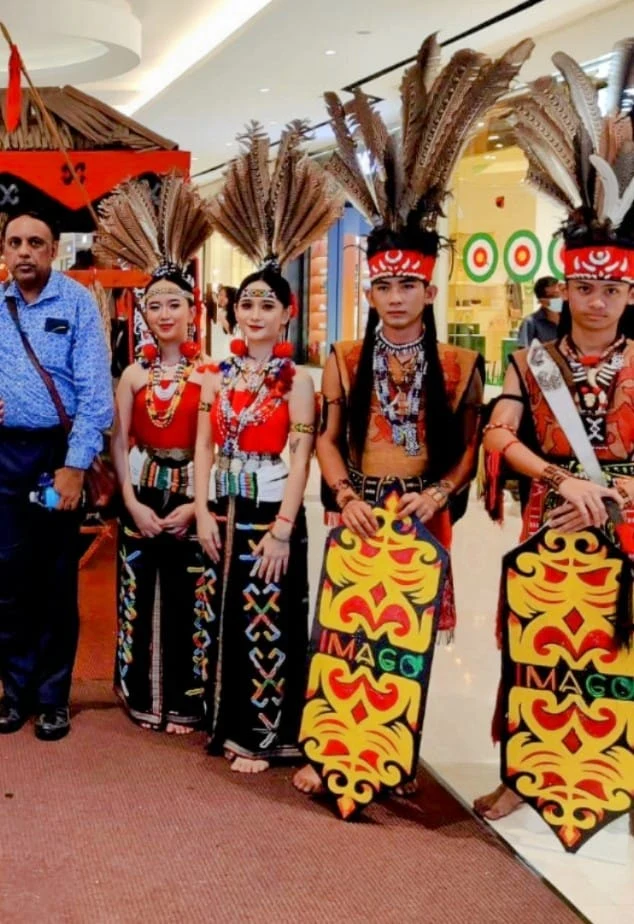 Male traveler posing with two indigenous warrior dancers holding traditional painted wooden shields