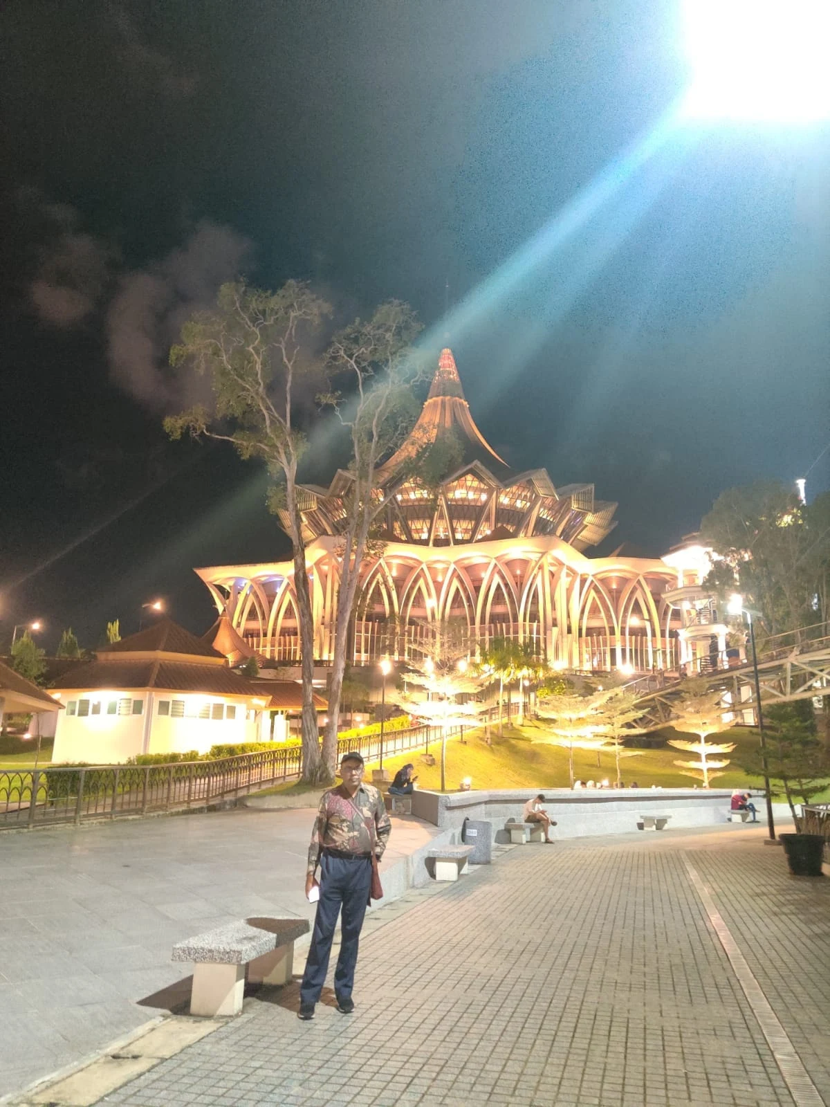 Male traveler on the Kuching Waterfront promenade at night with the majestic illuminated Sarawak State Legislative Assembly building glowing in the background