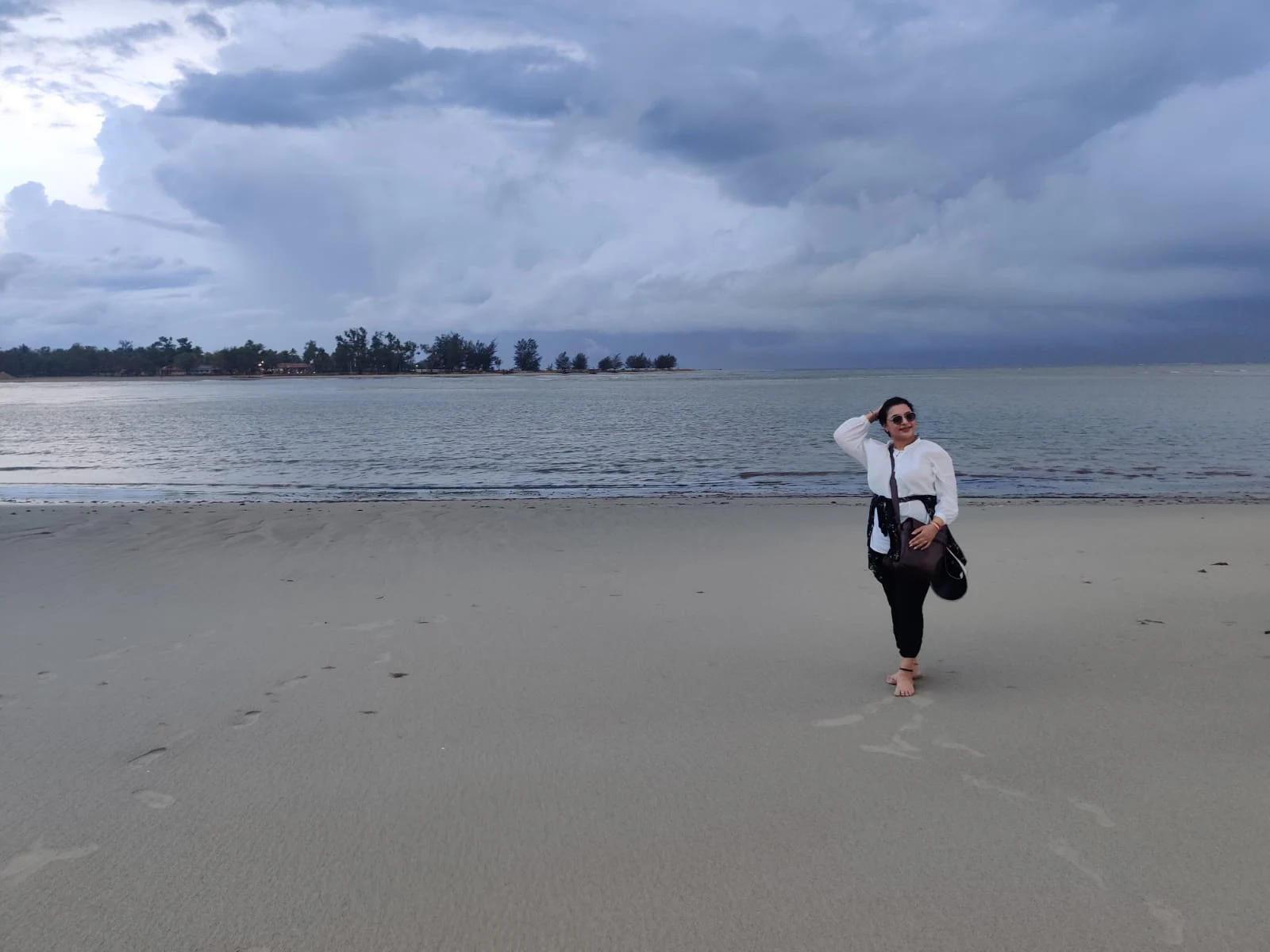 Female traveler standing barefoot on the vast sandy beach under dramatic skies in Sabah, Kota Kinabalu