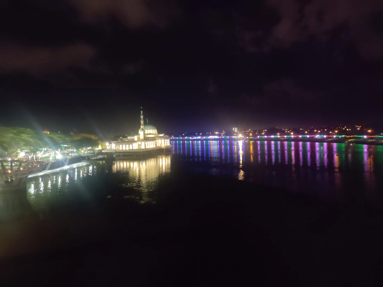 Night view of the Sarawak River with illuminated Masjid Terapung floating mosque reflecting golden light across the water