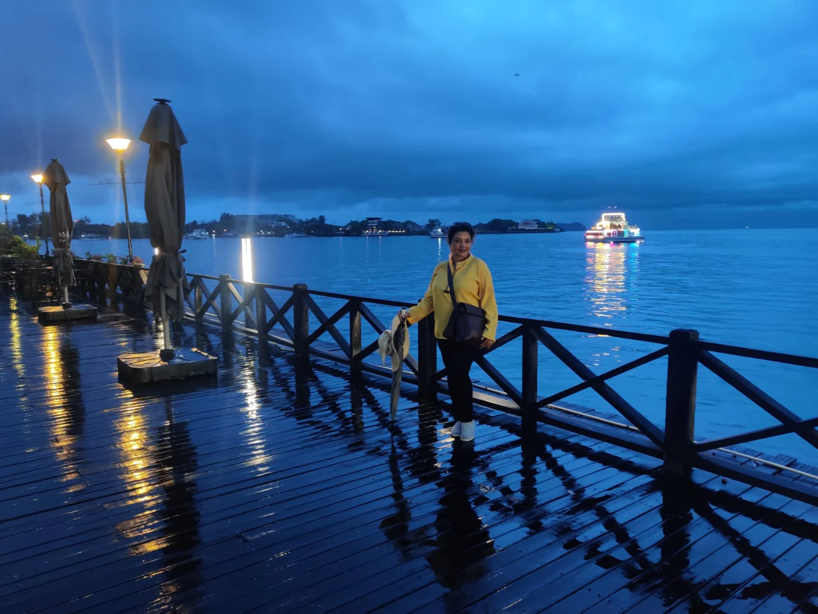 Female traveler in yellow standing on the wooden boardwalk pier overlooking the Borneo coastal waters at twilight