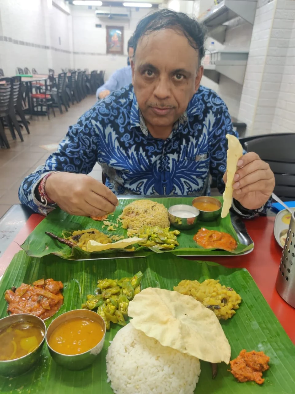 Male traveler enjoying an authentic South Indian banana leaf meal with rice, biryani, rasam, sambar, and papadum in Little India, Penang
