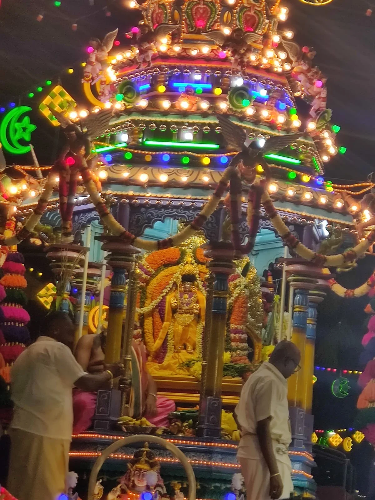 Close-up of the ornate ceremonial rath chariot enshrining the golden deity of Lord Murugan flanked by priests and marigold garlands