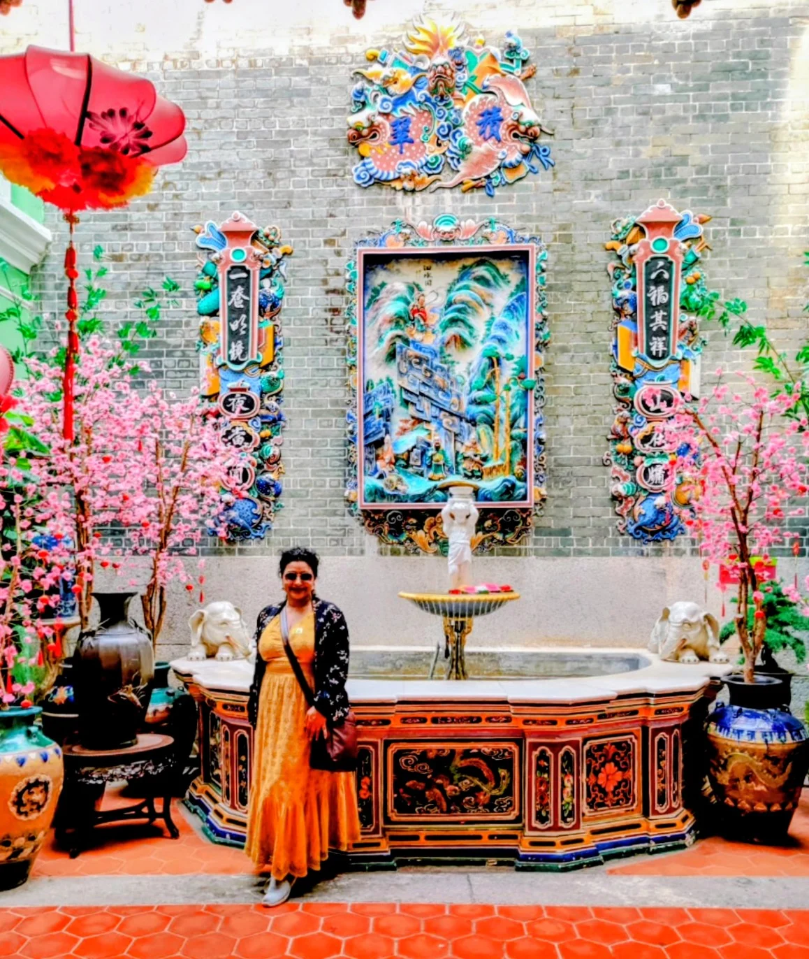 Female traveler standing in the ornate ceramic fountain courtyard of the Chinese heritage home