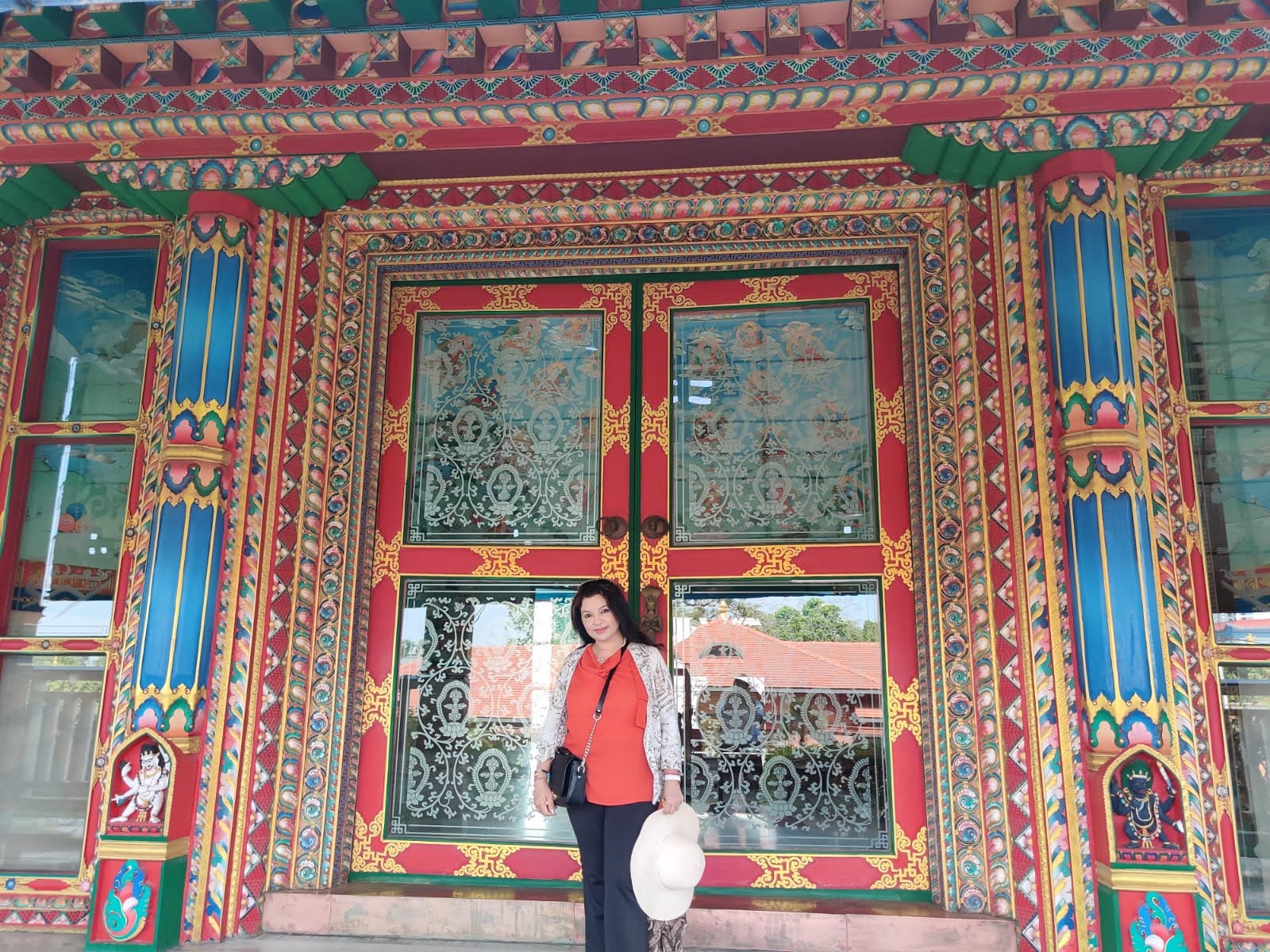 Traveler dressed in modest pilgrimage attire before the carved Tibetan doors of German Monastery