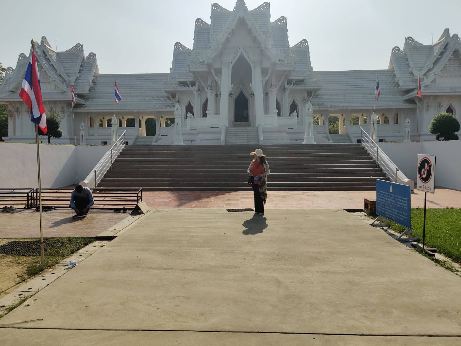 Grand white marble facade of the Royal Thai Monastery with Thai flags, multi-tiered gables, and wide ceremonial stairs