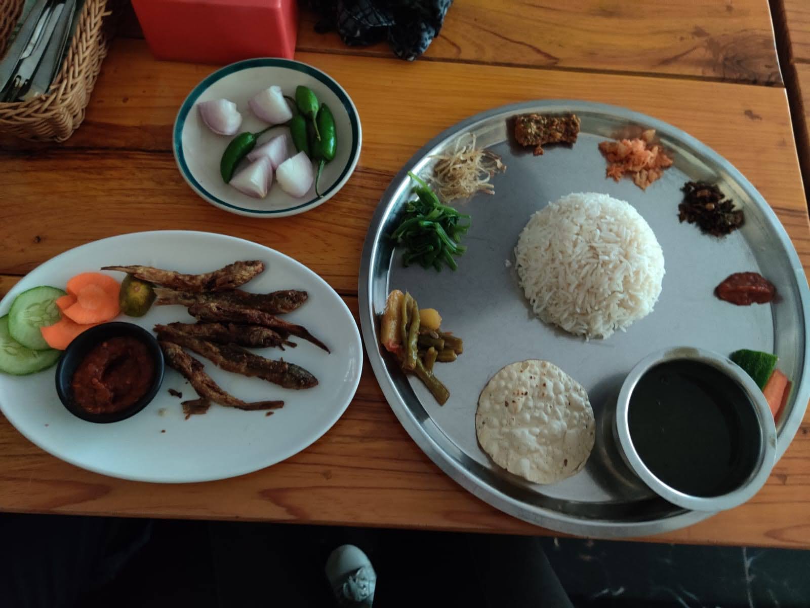 Traditional Thakali Thali platter served with steamed rice, black kalo dal, saag greens, fresh pickles, papad, raw chilies, and crispy fried fish