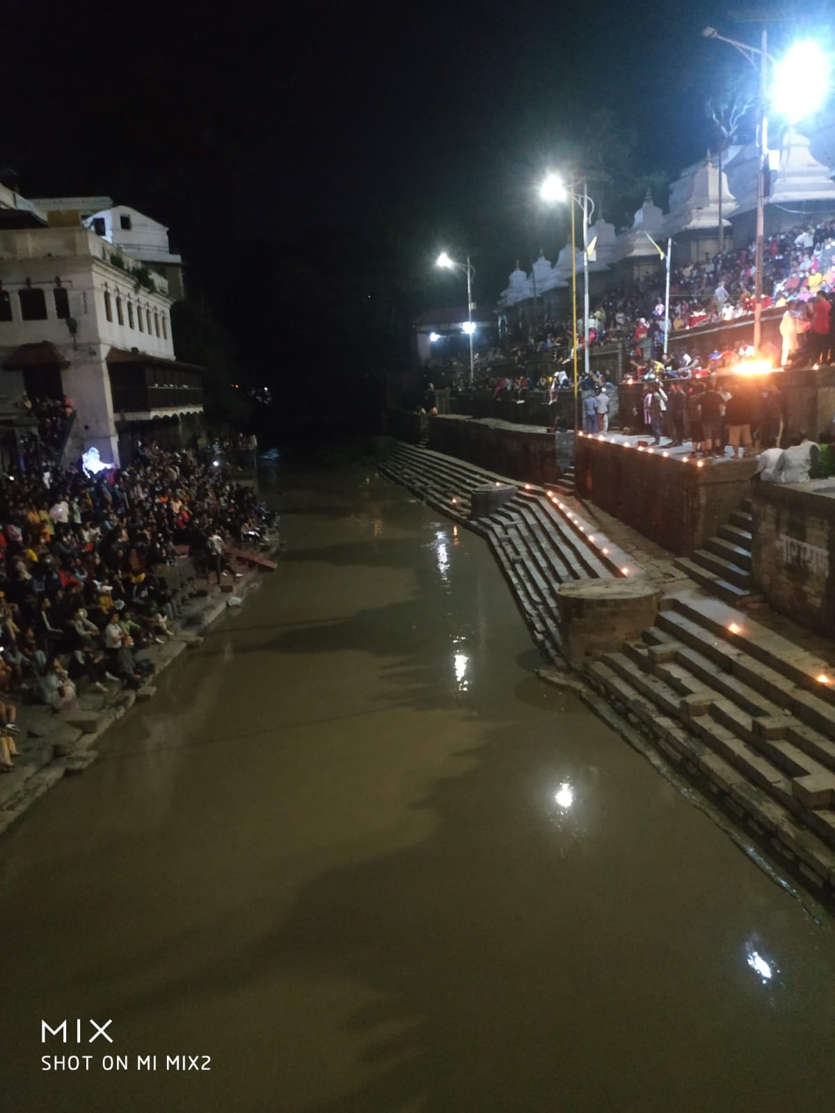 The sacred Bagmati River flowing past the stone Arya Ghats illuminated with evening lamps and gathering crowds