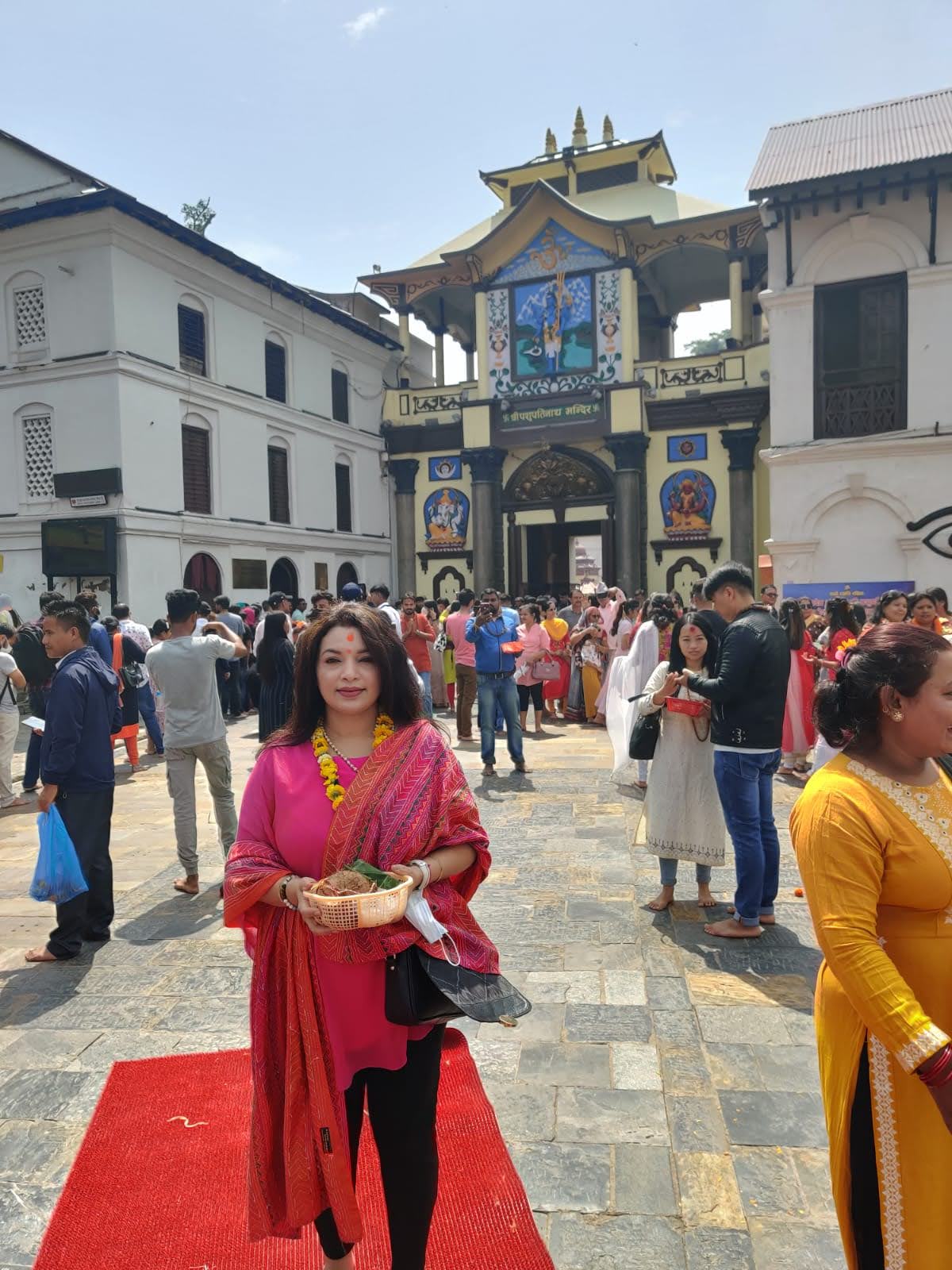 Returning devotee holding puja basket on the red carpet in front of the grand entrance gate of Pashupatinath Temple