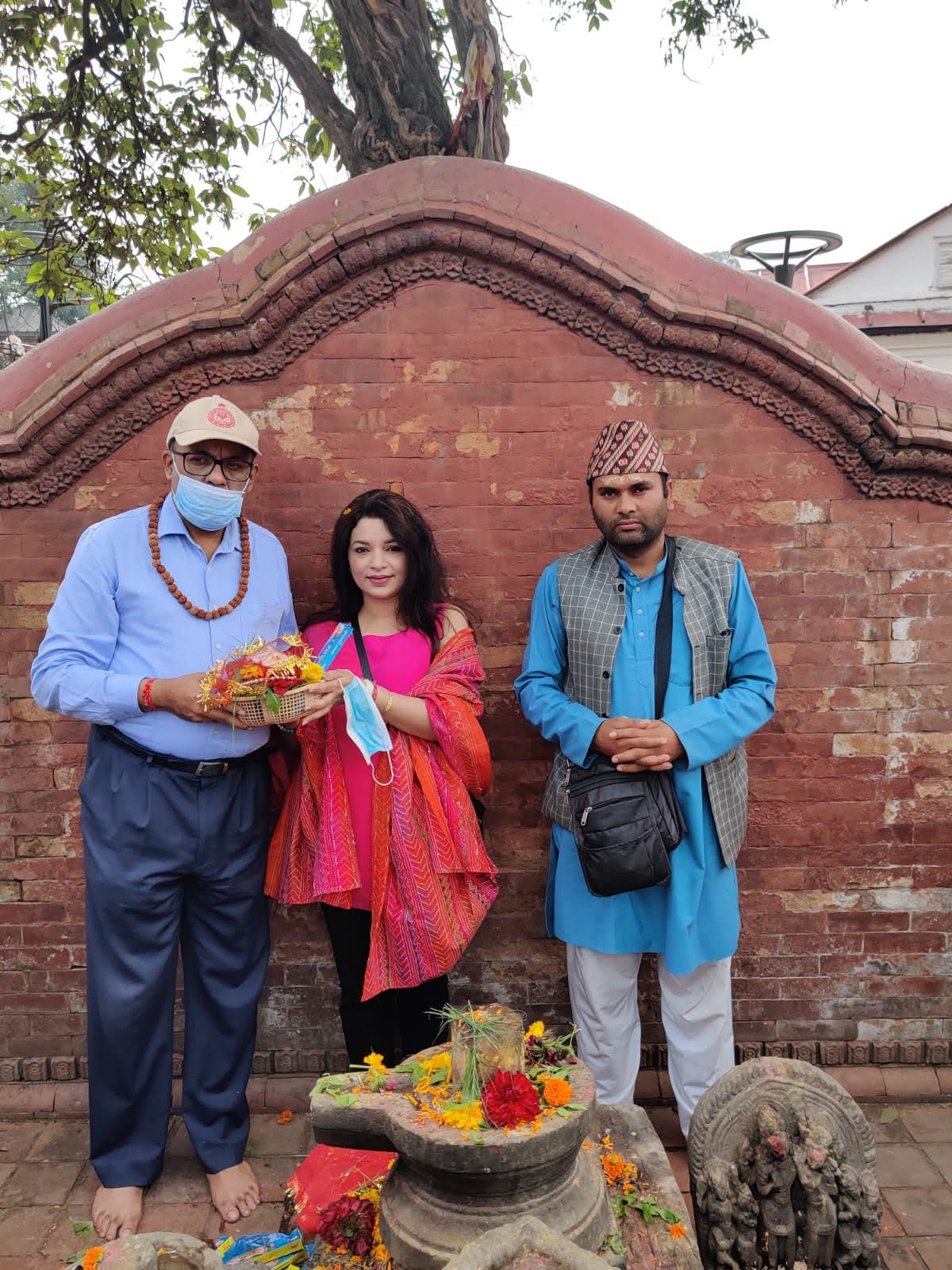 Travelers performing a traditional puja ceremony assisted by a local pandit at a stone Shivalinga decorated with flowers