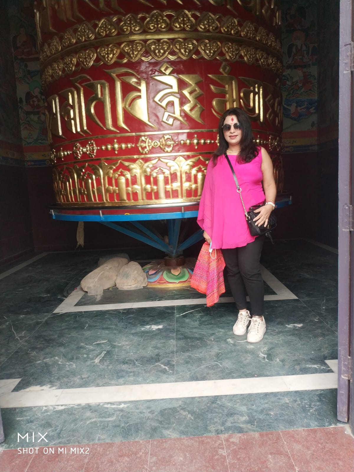 Traveler standing beside a massive golden and red Tibetan Mani prayer wheel inscribed with sacred mantras